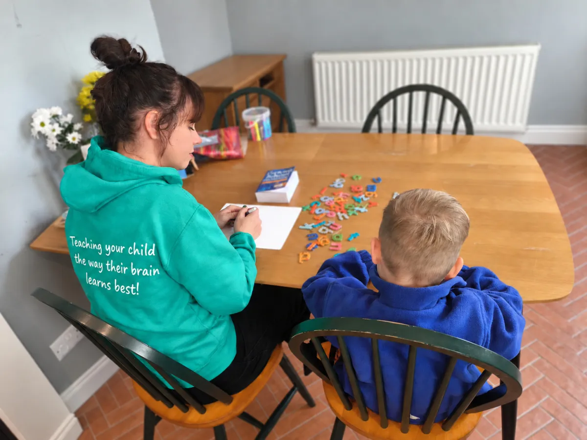Natalie, in a green Yorkshire Wolds Dyslexia Service hoodie reading 'Teaching your child the way their brain learns best!', working with a child and magnetic letters at a table